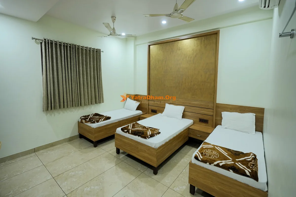 Triple bed AC room with wooden beds and curtains at Shree Harikrishna Bhuvan, Bhuj
